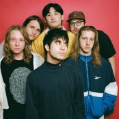 The six members of the band The Sophs in front of a red backdrop